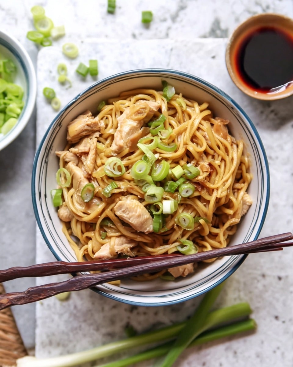 The image shows a white bowl with a blue rim filled with stir-fried noodles. The noodles are light brown and glossy, mixed with pieces of light brown cooked chicken and scattered slices of green onions on top. A pair of dark brown wooden chopsticks rests on the side of the bowl, lying across the noodles. The bowl sits on a white marbled surface, with scattered pieces of green onion around it. In the background, there is a small bowl of sliced green onions and a small cup with a dark red sauce nearby. Photo taken with an iphone --ar 4:5 --v 7