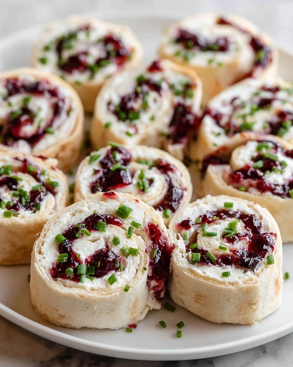 The image shows a white plate with multiple small spiral rolls arranged closely. Each roll has three visible layers: the outer layer is a light beige, soft flatbread, the middle layer is a spread of white creamy cheese, and the inner layer is a dark red jelly filling with a glossy texture and small whole berries. The rolls are topped and scattered with small chopped green herbs. The plate sits on a white marbled surface. photo taken with an iphone --ar 4:5 --v 7