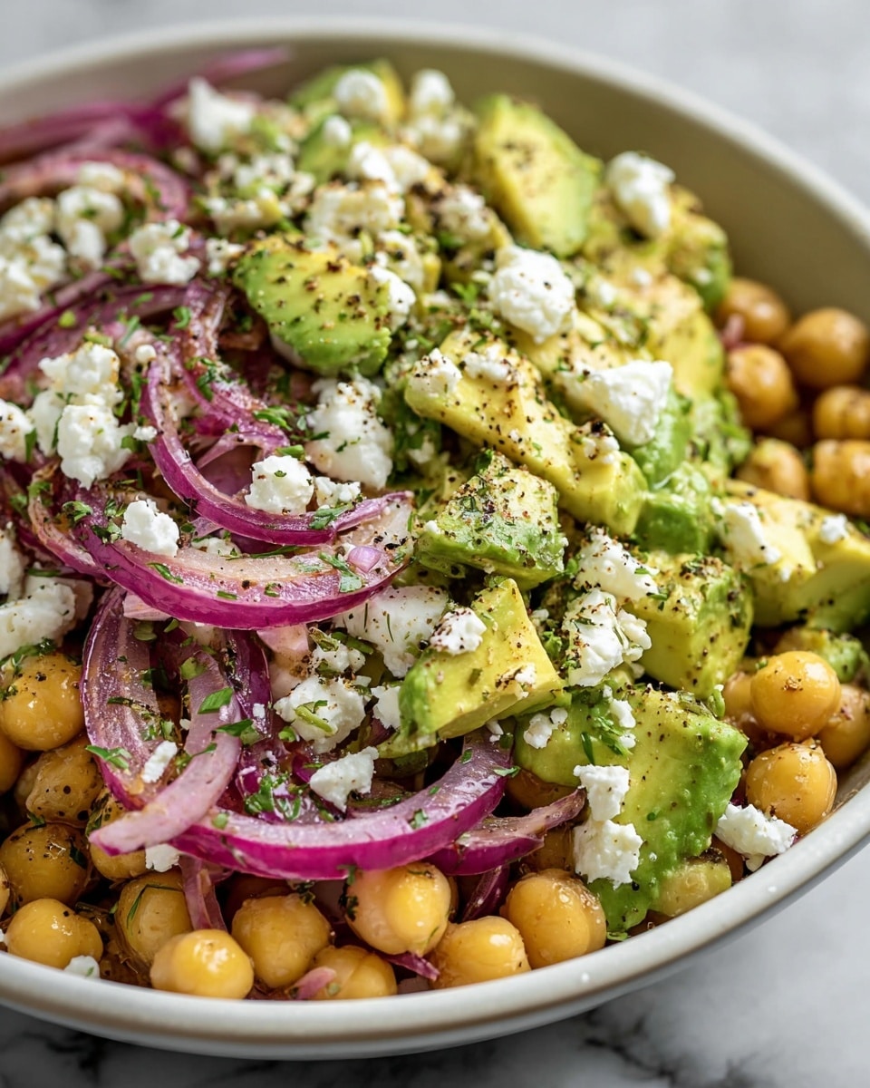 A close-up view of a salad in a white bowl showing three main layers: the bottom layer has soft yellow chickpeas, the middle layer contains bright green avocado chunks with creamy texture, and the top layer has thin slices of purple-red onion mixed with white crumbled cheese. The salad is sprinkled with chopped green herbs and black pepper, which add texture and contrast to the colors. The bowl is placed on a white marbled surface. Photo taken with an iphone --ar 4:5 --v 7