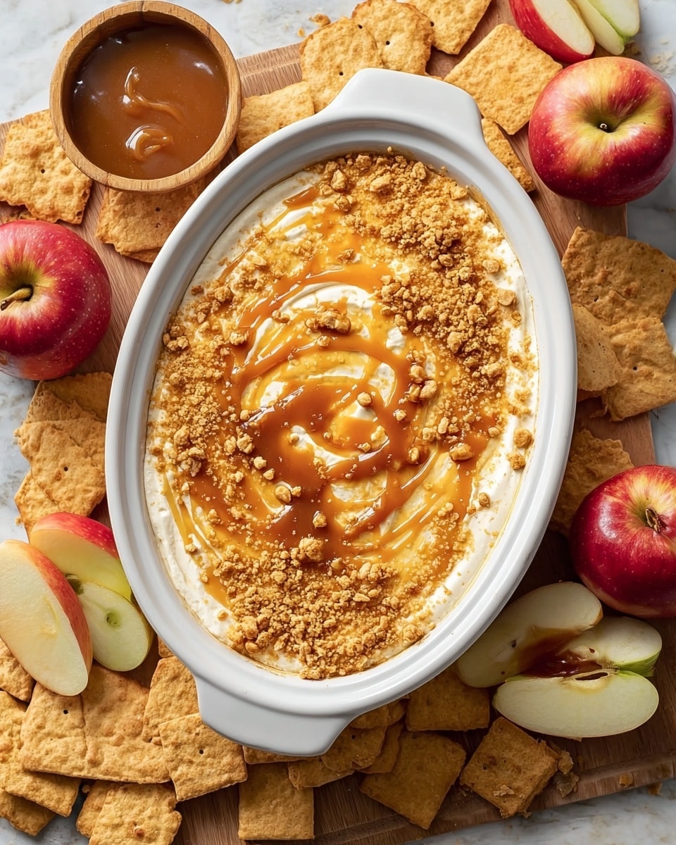 A white oval dish filled with a layered dip. The bottom layer is creamy white, smooth and thick, spread evenly across the base. The middle layer is a swirl of sticky caramel sauce, amber in color, spread over the white layer in a circular motion. The top layer is a sprinkling of crumbled golden yellow crunchy pieces evenly scattered to cover the surface. The dish is placed on a wooden board, around which are square tan crackers, some whole and some broken, scattered loosely. Red apples sit nearby, some whole with shiny red and green skin, and some sliced into wedges showing white flesh. There is a small wooden bowl filled with caramel sauce near the top left corner. The whole scene is on a white marbled texture surface. Photo taken with an iphone --ar 4:5 --v 7