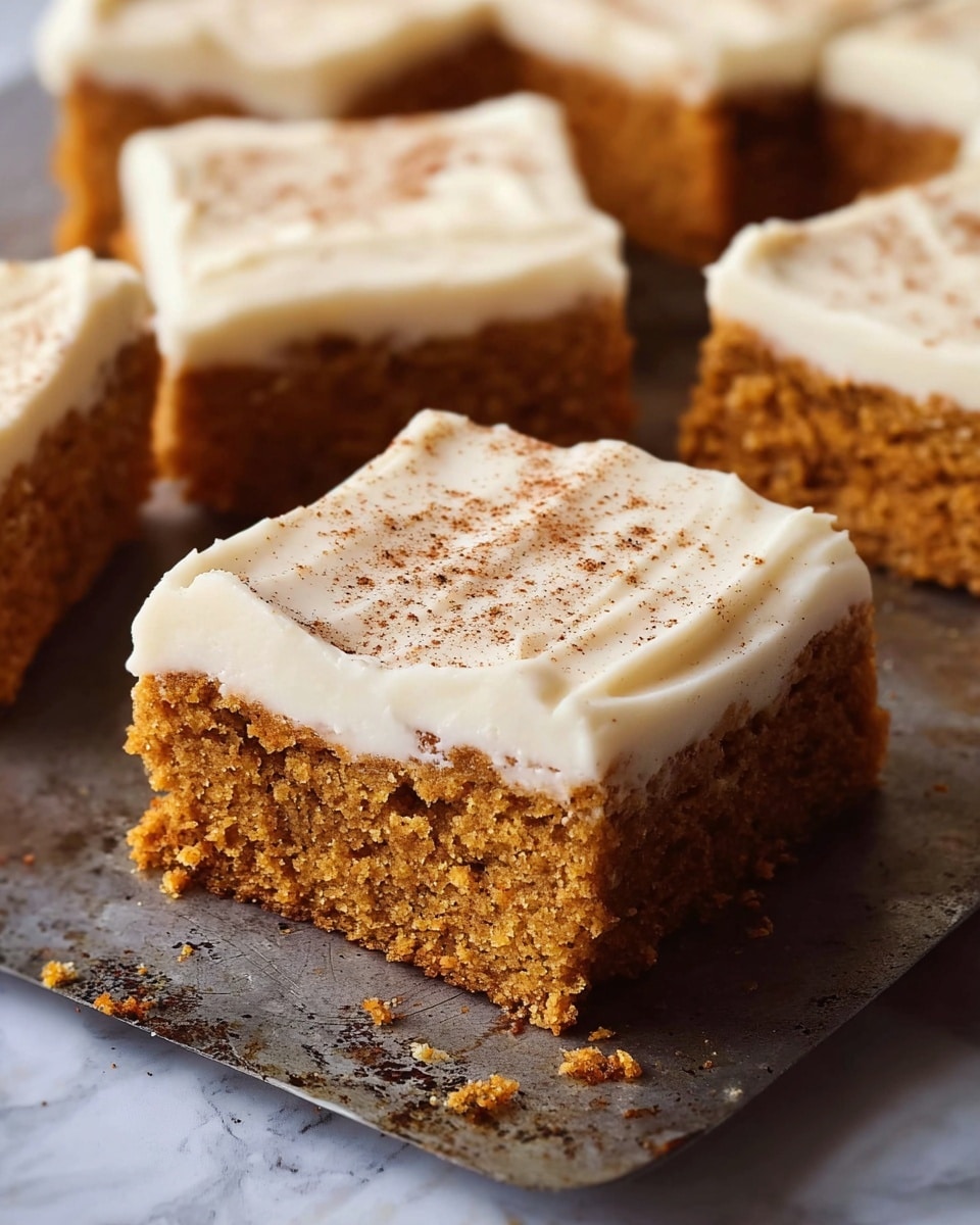The image shows several square pieces of moist carrot cake with a thick layer of smooth white cream cheese frosting on top, sprinkled lightly with brown cinnamon powder. The cake layer is dense and golden-brown with a crumbly, soft texture. The frosting layer is spread evenly with some gentle ridges, covering the entire top of each cake piece. The cakes are placed on a rustic metal baking tray with a slightly worn surface. The background is a white marbled texture photo taken with an iphone --ar 4:5 --v 7