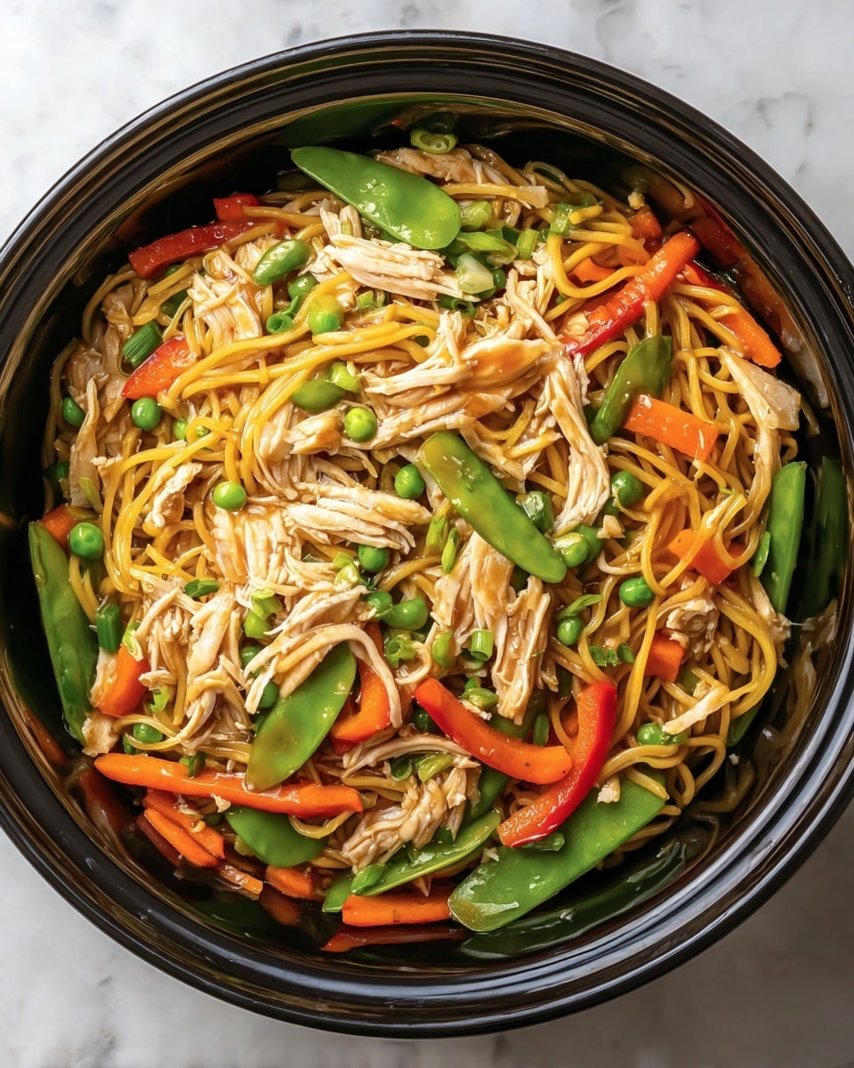 A close-up view of a black round bowl filled with a noodle dish. The first layer shows thin yellow noodles mixed with light brown shredded chicken evenly spread across the bowl. On top of the noodles and chicken are bright green snap peas, small green peas, orange carrot strips, and slices of red and green bell peppers, creating a colorful mix. The glossy sauce coats everything, making the ingredients look shiny and well-mixed. The bowl is placed on a white marbled surface. Photo taken with an iphone --ar 4:5 --v 7