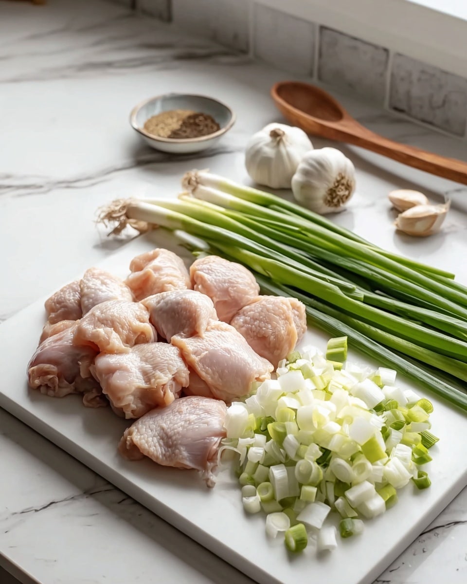 The image shows a white square plate on a white marbled surface with seven raw chicken pieces placed in two rows on the left side. To their right, there is a mound of chopped white and light green spring onions in the front, followed by whole green onions arranged parallel behind them. Near the green onions, there are several whole garlic cloves and a full garlic bulb. In the background, a small bowl holds some spices, and a wooden spoon rests on the counter next to it, all set against a white marbled countertop and tiled backsplash. Photo taken with an iphone --ar 4:5 --v 7