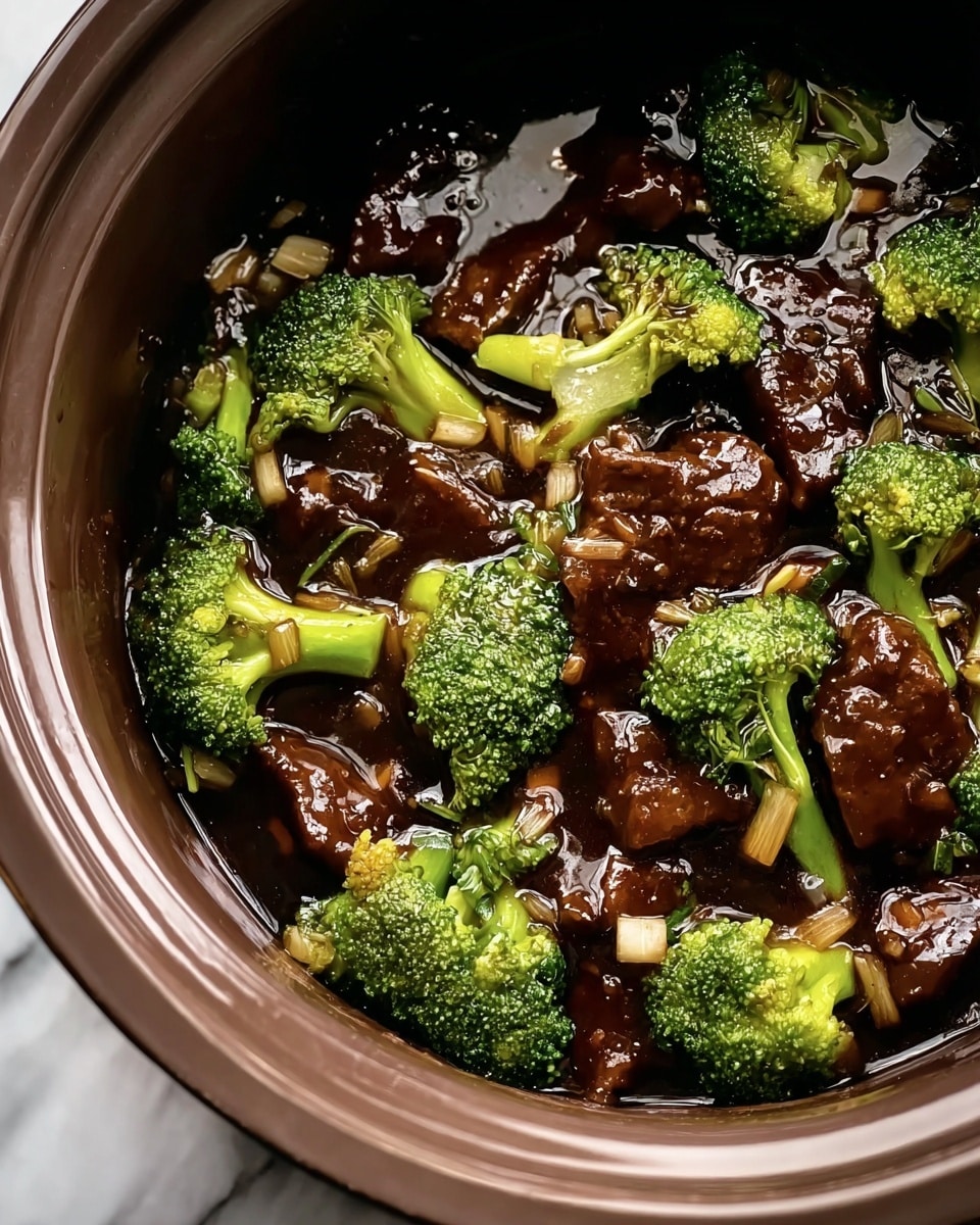 The image shows a close-up view of a dish inside a round cooking pot with a glossy surface. The dish has two main layers: bright green broccoli florets with a slightly rough texture, and thick, glossy pieces of dark brown beef coated with a shiny sauce. Small translucent diced onions are scattered among the broccoli and beef. The sauce is dark, rich, and shiny, covering the ingredients evenly. The pot is set against a white marbled surface. photo taken with an iphone --ar 4:5 --v 7