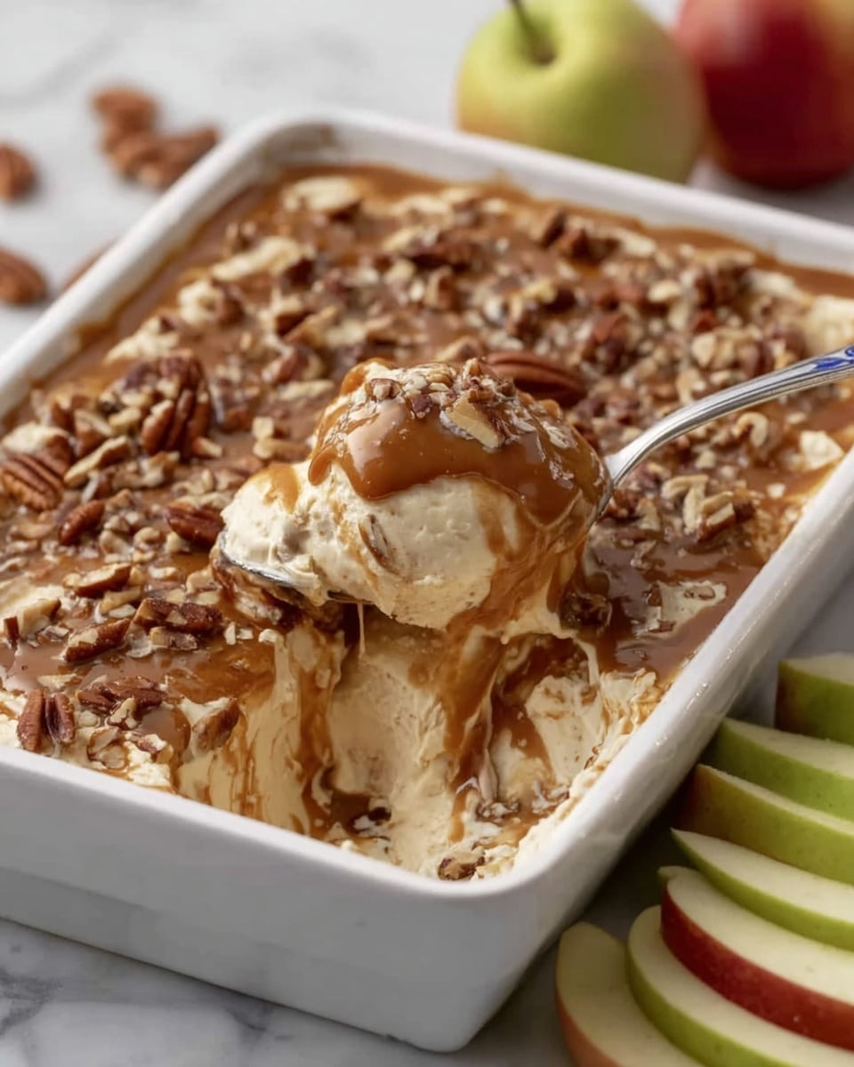 A white rectangular dish holds a creamy dessert with two distinct layers. The bottom layer is thick and light beige in color, with a smooth and slightly fluffy texture. The top layer is a darker brown, glossy sauce, generously sprinkled with small chunks of pecans. A spoon rests in the dish, scooping a portion that blends both layers, showing a mix of light beige cream with streaks of brown sauce. The dish is set on a white marbled surface with slices of green and red apples nearby. Photo taken with an iphone --ar 4:5 --v 7