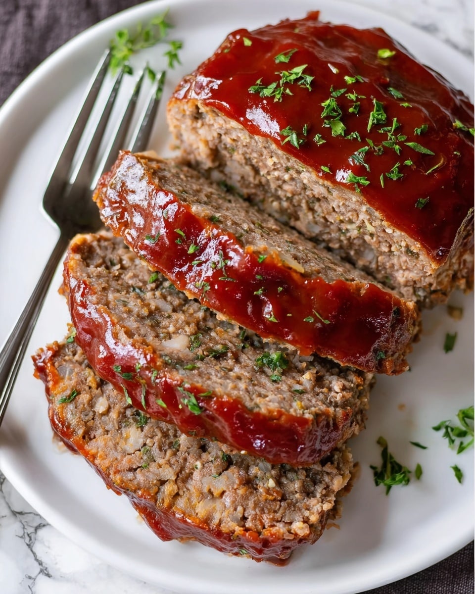 The image shows a meatloaf sliced into three thick pieces on a white plate. The top layer is a shiny reddish-brown sauce spread evenly over the meatloaf, slightly dripping down the sides. The meatloaf itself is a dense mix of ground meat and small bits of onion, with a brownish-gray color and a moist texture. Small green herb pieces are sprinkled on top of the sauce and around the meatloaf for garnish. A silver fork is placed on the left side of the plate, and the background is a white marbled surface. Photo taken with an iphone --ar 4:5 --v 7