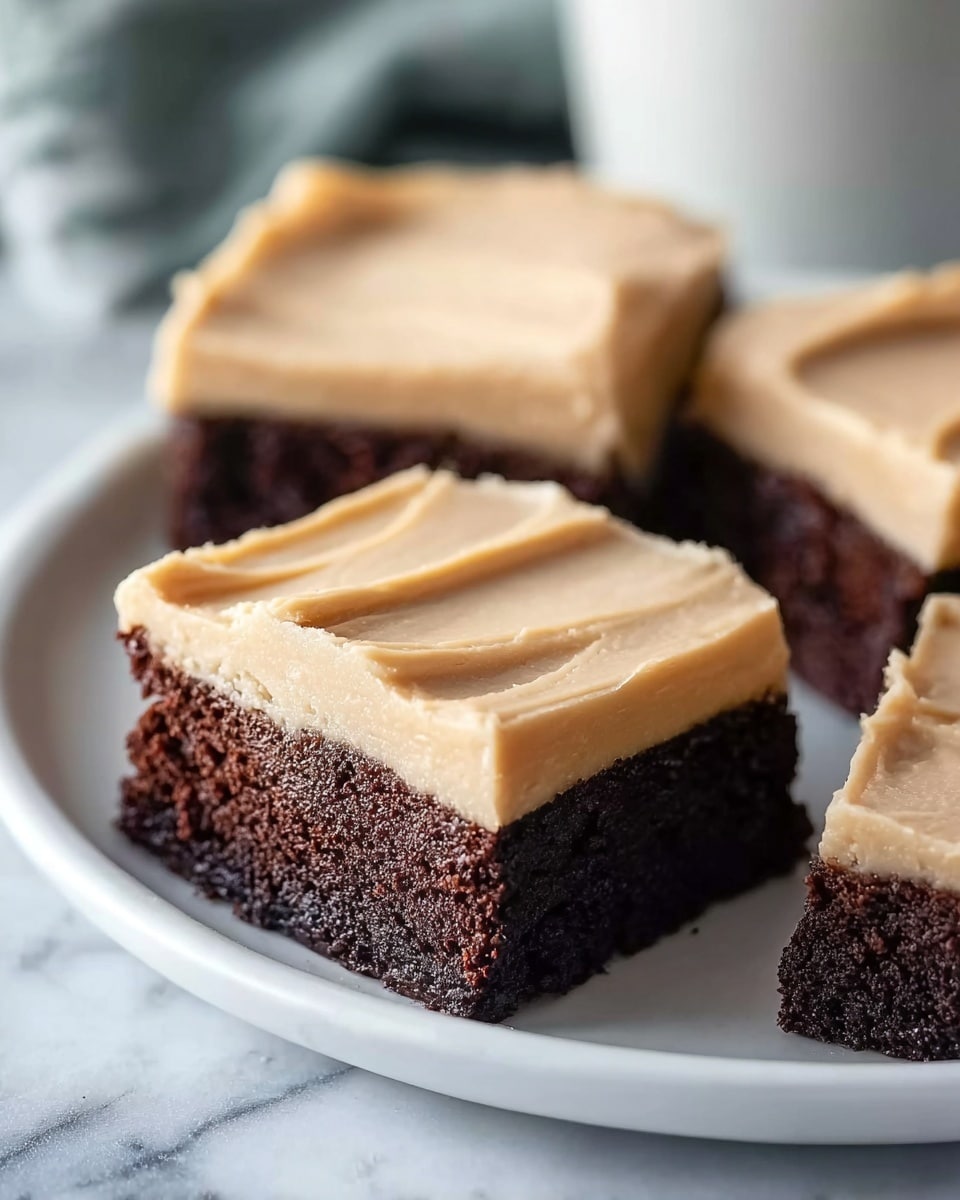 The image shows three square pieces of chocolate cake with a thick layer of light beige frosting on top. Each piece has one visible layer of dark, moist chocolate cake and one thick layer of smooth, creamy frosting with visible strokes on the surface. The cake pieces are arranged on a white plate that rests on a white marbled surface. The background is softly blurred, drawing focus to the close-up of the cake pieces. photo taken with an iphone --ar 4:5 --v 7