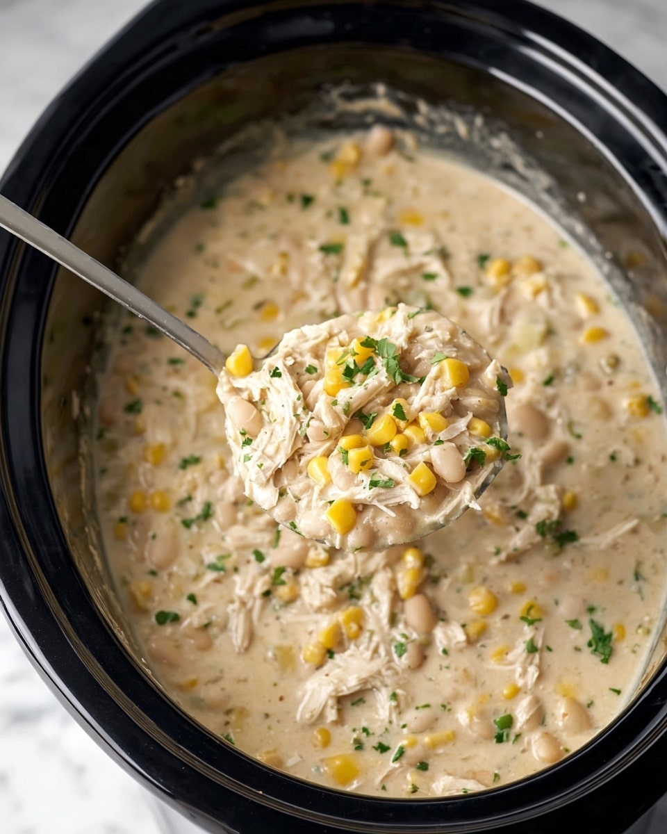 A close-up view of a creamy stew filled with shredded white chicken, small yellow corn kernels, and white beans in a black slow cooker. The stew is thick and pale beige in color with bits of chopped green herbs sprinkled throughout. A spoon lifts some stew, showing the mix of chicken shreds, corn, beans, and herbs clearly. The background is a white marbled surface. Photo taken with an iphone --ar 4:5 --v 7