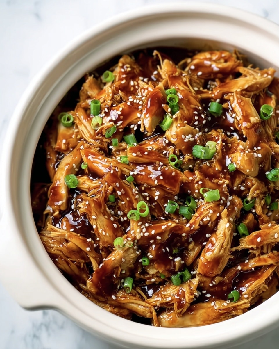 The image shows a white ceramic bowl filled with shredded chicken pieces coated in a shiny brown sauce. The chicken pieces are layered unevenly, glistening with the thick sauce. Small white sesame seeds are sprinkled on top, adding texture. Bright green chopped scallions are scattered across the dish, giving a fresh contrast to the deep brown chicken. The bowl sits on a white marbled surface. photo taken with an iphone --ar 4:5 --v 7