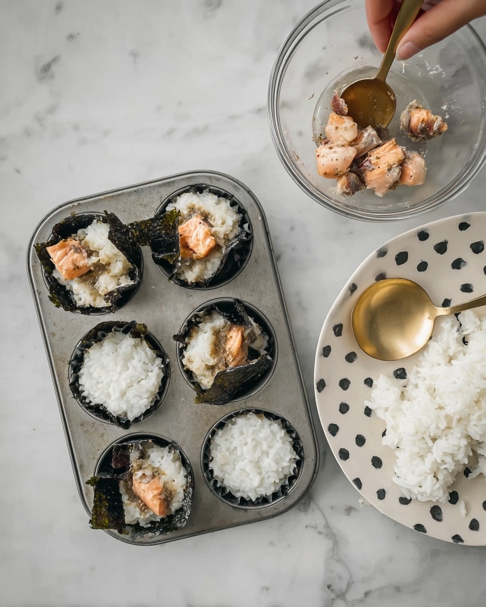 The image shows a metal muffin tray on a white marbled surface, with three compartments partially filled with small cups made from dark seaweed. Inside two of the seaweed cups are layers of white rice on the bottom and chunks of light brown marinated fish on top. The third seaweed cup contains only white rice. Next to the tray is a white plate with large black dots, holding a pile of white rice and a golden spoon resting on top. Above these items, a glass bowl contains pieces of light brown marinated fish, with a golden spoon inside. A woman's hand is just out of frame, about to mix the fish in the bowl. photo taken with an iphone --ar 4:5 --v 7
