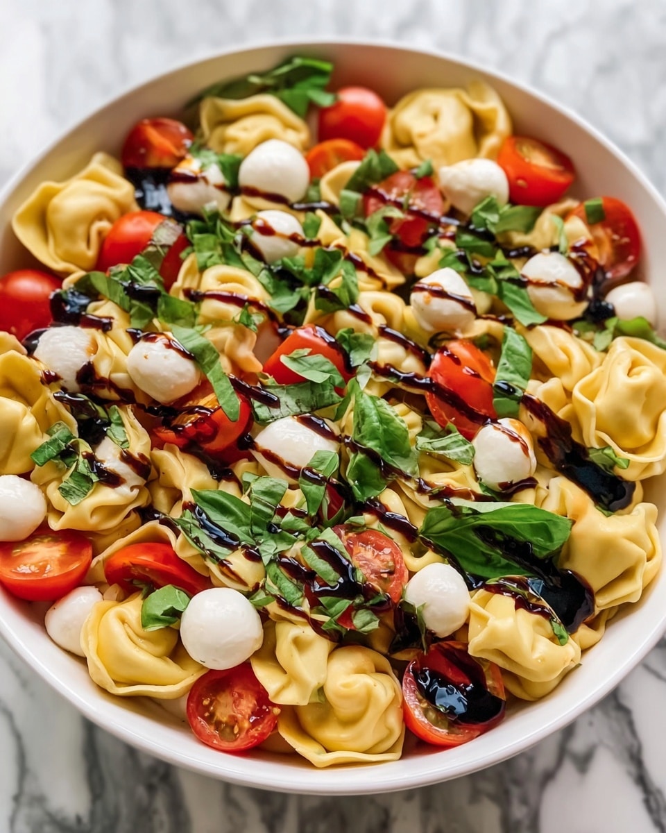 A white bowl is filled with three layers of food starting with light yellow tortellini pasta at the bottom, showing smooth and folded textures. On top of it, there are bright red cherry tomato halves scattered evenly around with small, smooth white mozzarella balls. The top layer has fresh green basil leaves that are roughly chopped, adding a pop of color and texture all over. A dark balsamic glaze is drizzled in thin lines over the whole dish giving it a shiny, rich contrast. The bowl sits on a white marbled background. photo taken with an iphone --ar 4:5 --v 7
