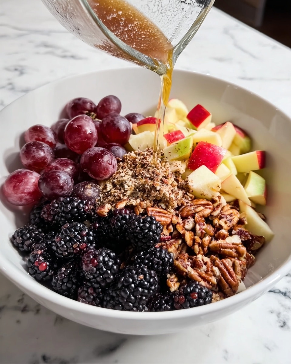 A white bowl with four layers of food sits on a white marbled surface. The first layer at the bottom is made of small red grapes on the left side. The second layer, covering the top right, consists of small pieces of red and yellow apple. The third layer in the center is a pile of chopped pecans with rough brown texture. The fourth layer at the front left is a cluster of large blackberries, shiny and bumpy. A clear glass container tilted above the bowl pours a brown liquid dressing over the ingredients. Photo taken with an iphone --ar 4:5 --v 7