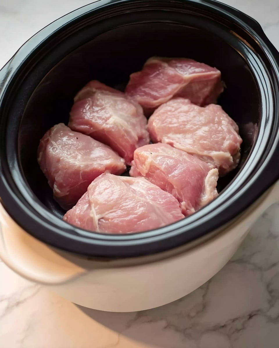 The image shows five raw pieces of light pink meat placed closely together inside a black slow cooker with a white outer casing. The slow cooker is sitting on a surface with a white marbled texture, and the scene is lit by soft natural lighting, highlighting the smooth and moist texture of the meat. The photo taken with an iphone --ar 4:5 --v 7