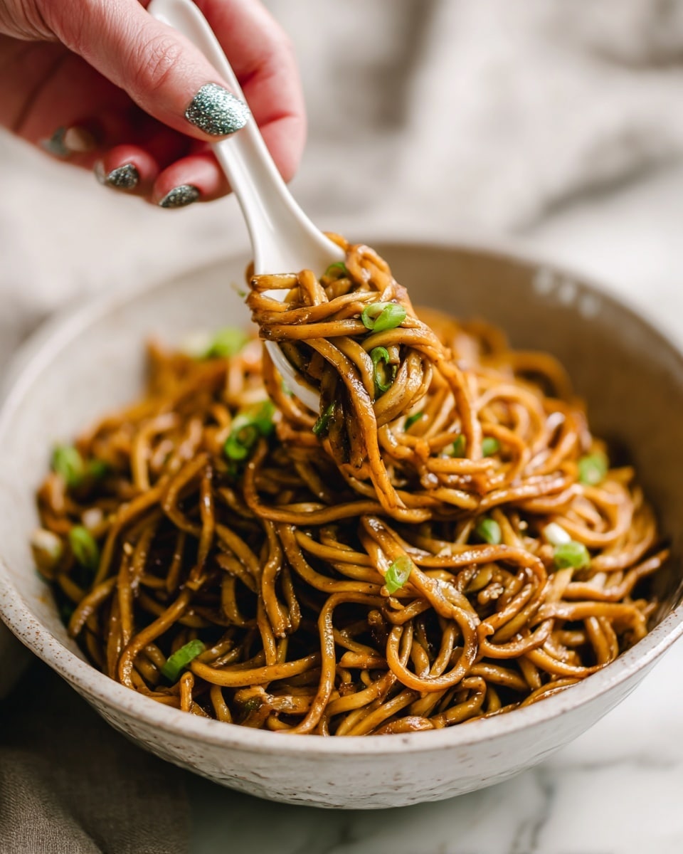 A close-up shows a bowl filled with thick, long, brown noodles that look glossy and slightly oily, mixed with small green onion pieces scattered on top, all sitting on a white marbled surface. A white ceramic spoon holds a small portion of the noodles above the bowl, with a woman's hand holding the spoon showing nails painted in soft purple and glittery silver polish. The background is softly blurred to keep focus on the noodles and the spoon photo taken with an iphone --ar 4:5 --v 7