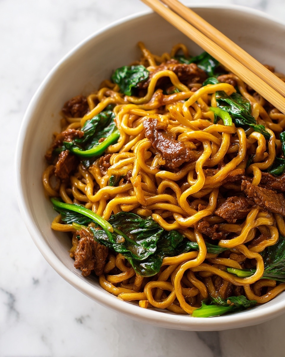 A white plate holds a serving of stir-fried thick yellow noodles coated in a glossy dark brown sauce, mixed evenly with small pieces of tender dark brown meat and bright green leafy vegetables. The noodles are twisted and tangled, creating a textured surface with a sauce sheen. On the top right side of the plate, a pair of light wooden chopsticks rests diagonally, partly touching the noodles. The plate is set on a white marbled surface with a soft blue and green checkered cloth partially visible in the background, along with orange flowers adding a splash of color. photo taken with an iphone --ar 4:5 --v 7