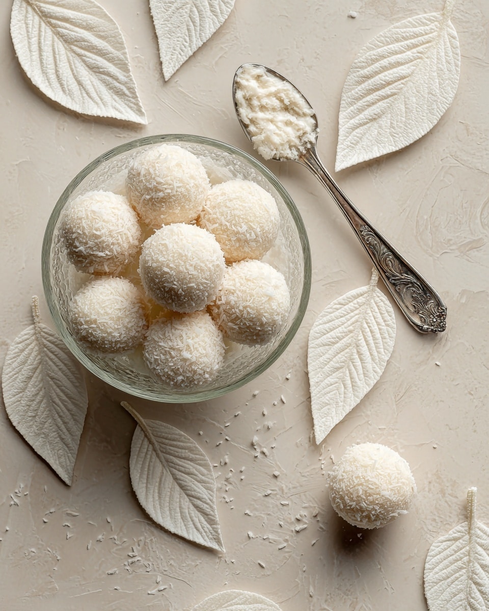 The image shows a glass bowl on the left side filled with round white coconut-covered balls. Around the bowl on the light brown surface, there are multiple white leaf-shaped pieces with smooth textures and clear vein details. A silver spoon with some white cream residue inside rests above the leaves, slightly tilted. One coconut ball is outside the bowl on the right side. The surface is changed to a white marbled texture. photo taken with an iphone --ar 4:5 --v 7