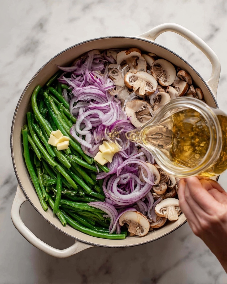 A top view of a white pot filled with three layers of ingredients: at the bottom, bright green whole green beans; in the middle, a layer of light brown sliced mushrooms with cream interiors; on top, a scattered layer of thinly sliced purple-red onions with white rings inside. There are small yellow pats of butter placed on the onions. A woman's hand is pouring a clear golden liquid from a small glass jar over the ingredients. The pot is set on a white marbled surface. Photo taken with an iphone --ar 4:5 --v 7