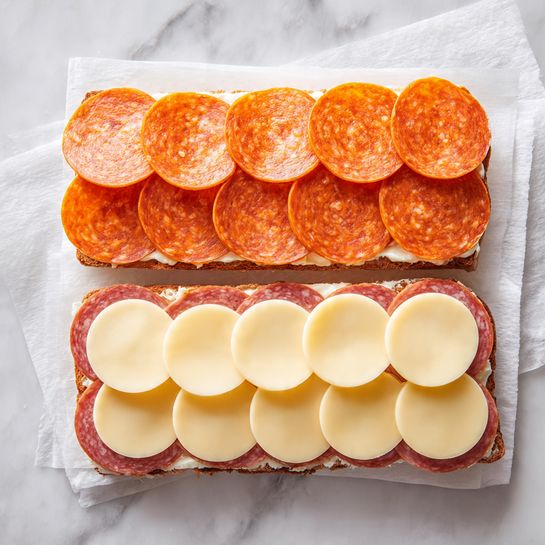 The image shows two open sandwich halves on a piece of white paper over a white marbled surface. The top half has three neat rows of bright orange slices with a firm texture, covering the bread fully and evenly. The bottom half has two rows of light yellow smooth round cheese slices, overlapping slightly to form a full layer over the bread. The bread edges are clearly visible around both layers. Photo taken with an iphone --ar 4:5 --v 7