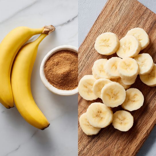 The image shows two parts: on the left, there are two whole green bananas placed side by side on a white marbled surface with a small white bowl filled with brown sugar and a sprinkle of cinnamon next to them; on the right, several slices of banana are arranged randomly on a wooden cutting board. The banana slices are oval-shaped with a pale creamy color and some light brown spots in the center. Photo taken with an iphone --ar 4:5 --v 7