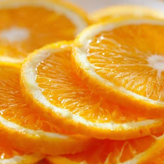 The image shows several fresh orange slices stacked closely together. Each slice has a bright orange rind with a slightly textured outer layer, and the inside is a translucent, juicy orange color with visible small segments and pulp. The slices are arranged so the curved rind edges form a repeating pattern. The surface beneath appears to be a white marbled texture. Photo taken with an iphone --ar 4:5 --v 7