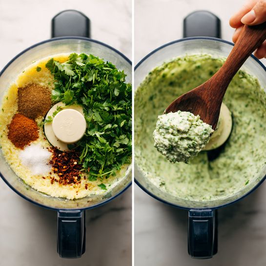 The image shows two views of a clear food processor bowl on a black base set on a white marbled surface. On the left, inside the bowl, there is a base layer of light yellow mixed ingredients, topped with fresh green cilantro covering most of the surface. On top of the cilantro, there are three small piles: one of brown ground spices, one of coarse white salt, and a small amount of dark red chili flakes. On the right, the food processor bowl contains a fully mixed pale greenish paste with bits of green herbs visible. A woman's hand holds a dark wooden spoon scooping up some of the mixture, showing its coarse but moist texture. Photo taken with an iphone --ar 4:5 --v 7