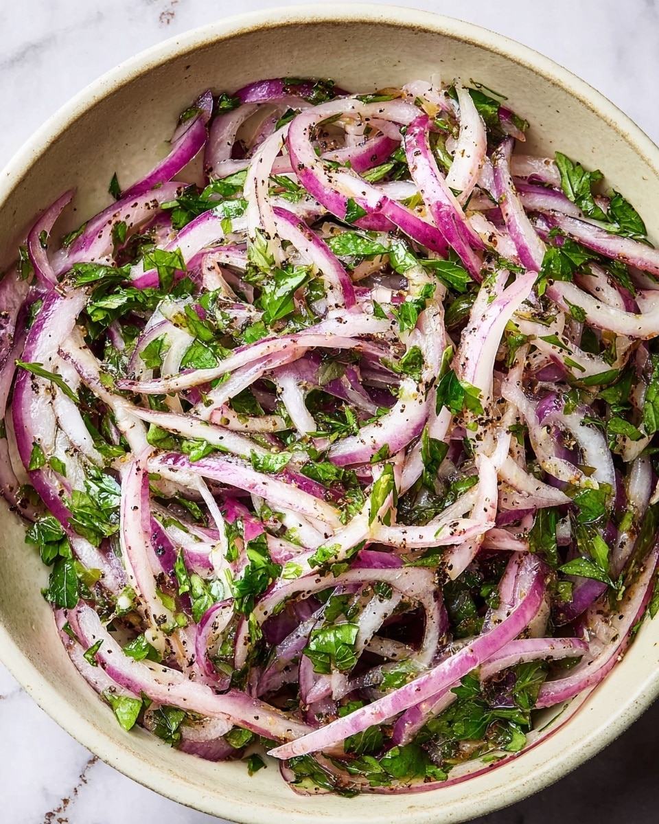 A white bowl filled with a mix of thinly sliced red and white onions, sprinkled with small green herb pieces, and light reddish-brown seasoning scattered evenly on top. The onions are layered loosely and look fresh and slightly shiny. Two tarnished silver forks rest on the right side of the bowl, partially placed inside. The bowl sits on a light wooden board with a jar of dark reddish spice labeled