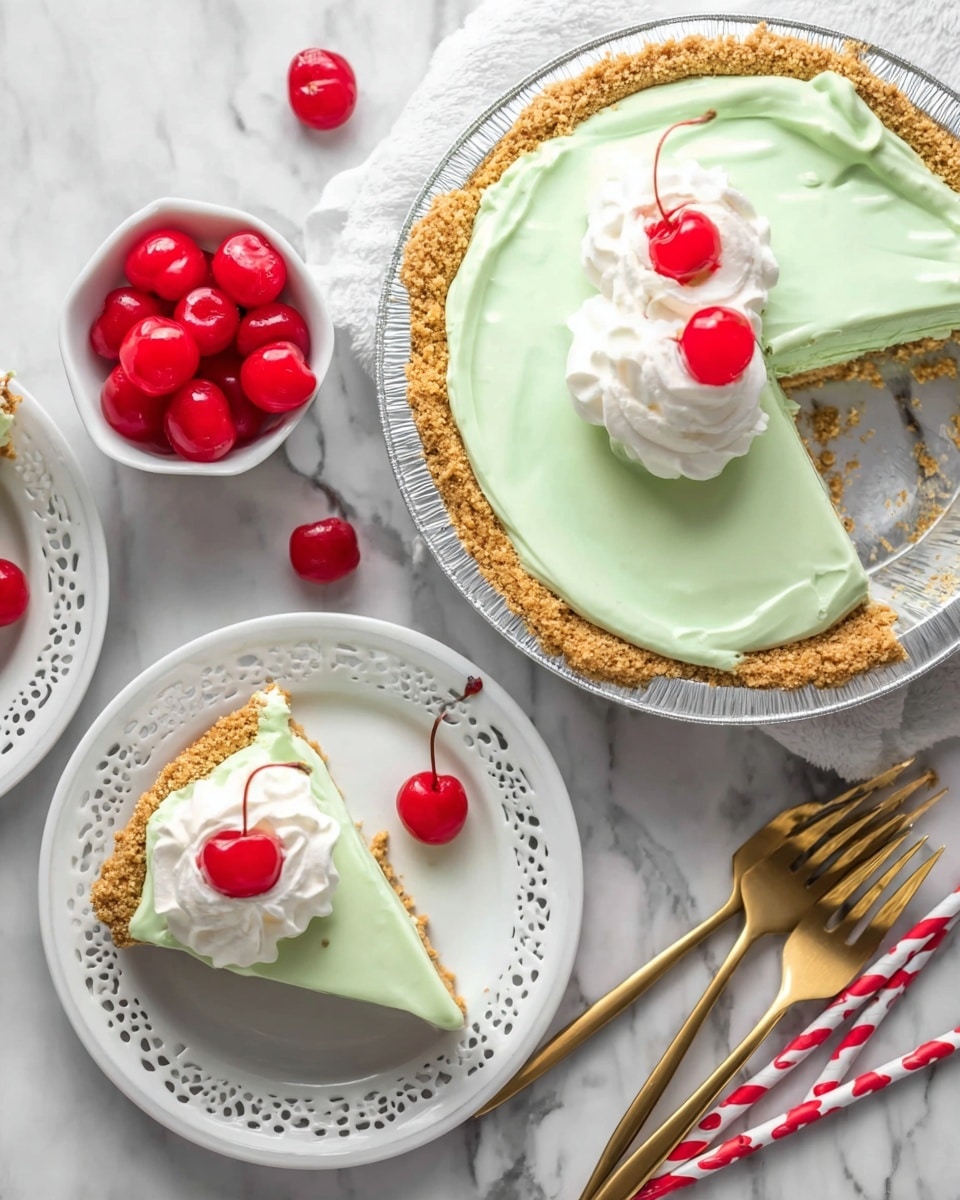 A single slice of light green pie sits on a white plate with a decorative edge. The pie has two layers: a crumbly, golden-brown crust at the bottom and a thick, smooth, light green filling on top. On the filling, there is a swirl of white whipped cream topped with a bright red cherry that has a long stem. The plate is on a white marbled surface with small crumbs around it. In the background, there are out-of-focus gold forks and a white bowl filled with more red cherries. photo taken with an iphone --ar 4:5 --v 7