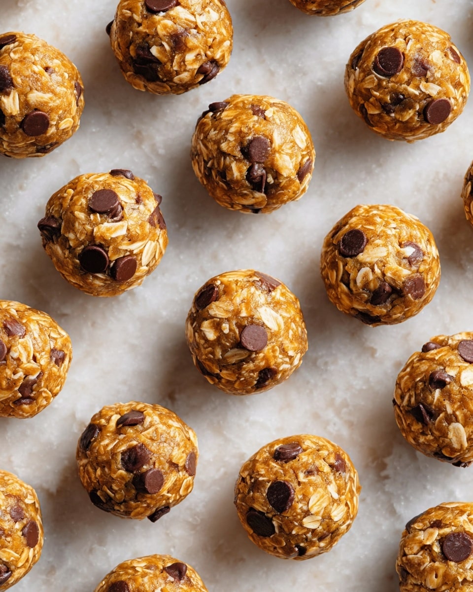 The image shows many small round energy bites laid out on a white marbled surface. Each bite is made of oats and has a golden-brown color with smooth sticky texture holding the oats together. There are many dark brown chocolate chips mixed into each bite, scattered on the surface. The bites are evenly spaced, and the light makes them look fresh and slightly shiny. photo taken with an iphone --ar 4:5 --v 7