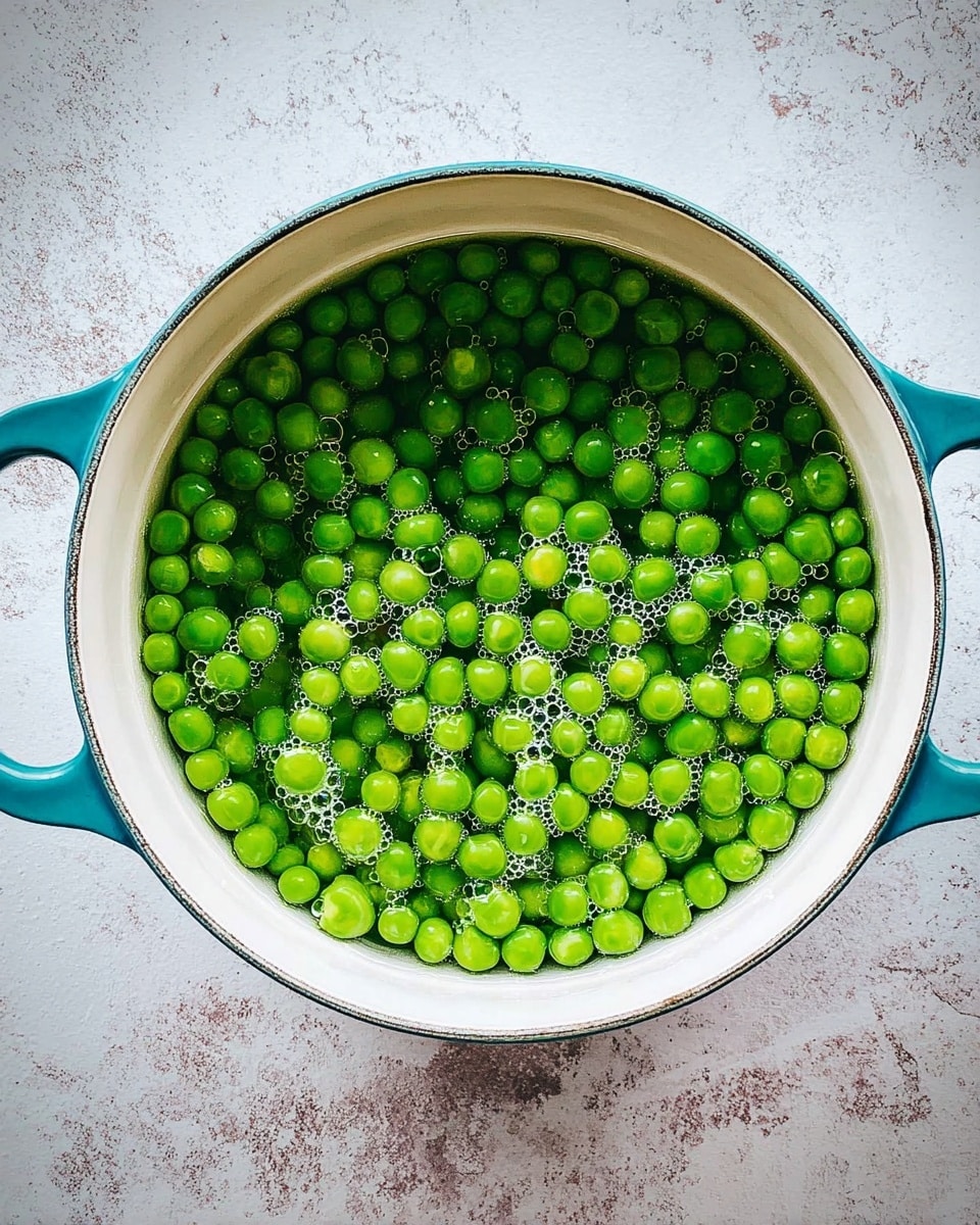 A top view of a white pot with teal handles filled with bright green peas submerged in clear water with small bubbles on the surface, placed on a white marbled texture background photo taken with an iphone --ar 4:5 --v 7