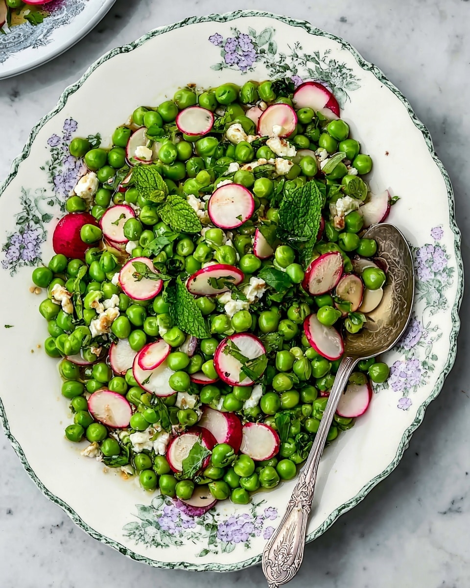 A white plate with floral edges holds a fresh green pea and thin radish slice salad. The dish has one main layer of bright green peas mixed with thin, round radish slices with red edges and white centers. Small bits of white cheese and chopped fresh herbs are scattered throughout. Bright green mint leaves add extra color on top. A silver spoon with engraved patterns rests on the right side of the plate, partly under the salad. The plate sits on a white marbled surface. Photo taken with an iphone --ar 4:5 --v 7