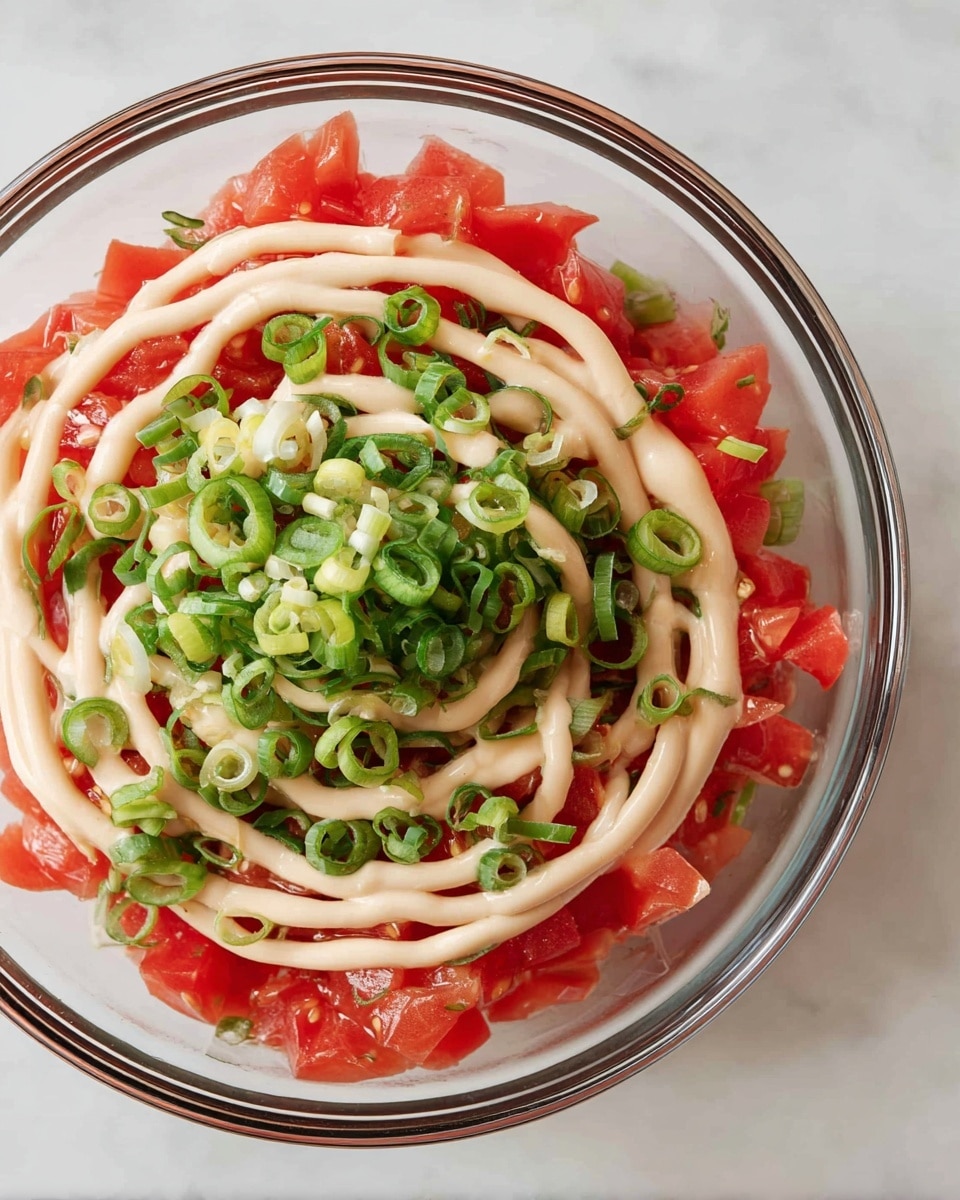 The image shows a clear glass bowl with three main layers inside. The bottom layer is bright red pieces of diced tomatoes spread evenly. On top of this is a layer of finely sliced green onions, adding a fresh green color and texture. The top layer is a spiral of creamy light beige sauce drizzled evenly over the green onions and tomatoes. The bowl sits on a white marbled surface. photo taken with an iphone --ar 4:5 --v 7