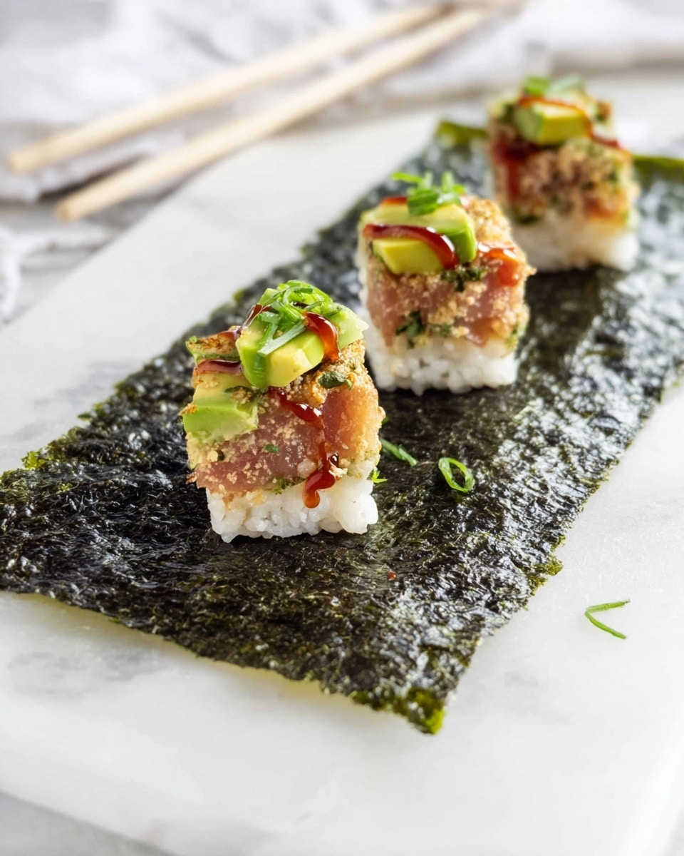 The image shows three small sushi pieces placed on a long sheet of dark green seaweed with a rough texture. Each sushi piece has a thick white rice base, topped with a mix of light brown tuna and small green avocado chunks. There are thin red sauce lines and small green onion bits scattered on top of each piece, adding bright color and contrast. The seaweed rests on a white marbled surface, with chopsticks and a white cloth in the background. Photo taken with an iphone --ar 4:5 --v 7