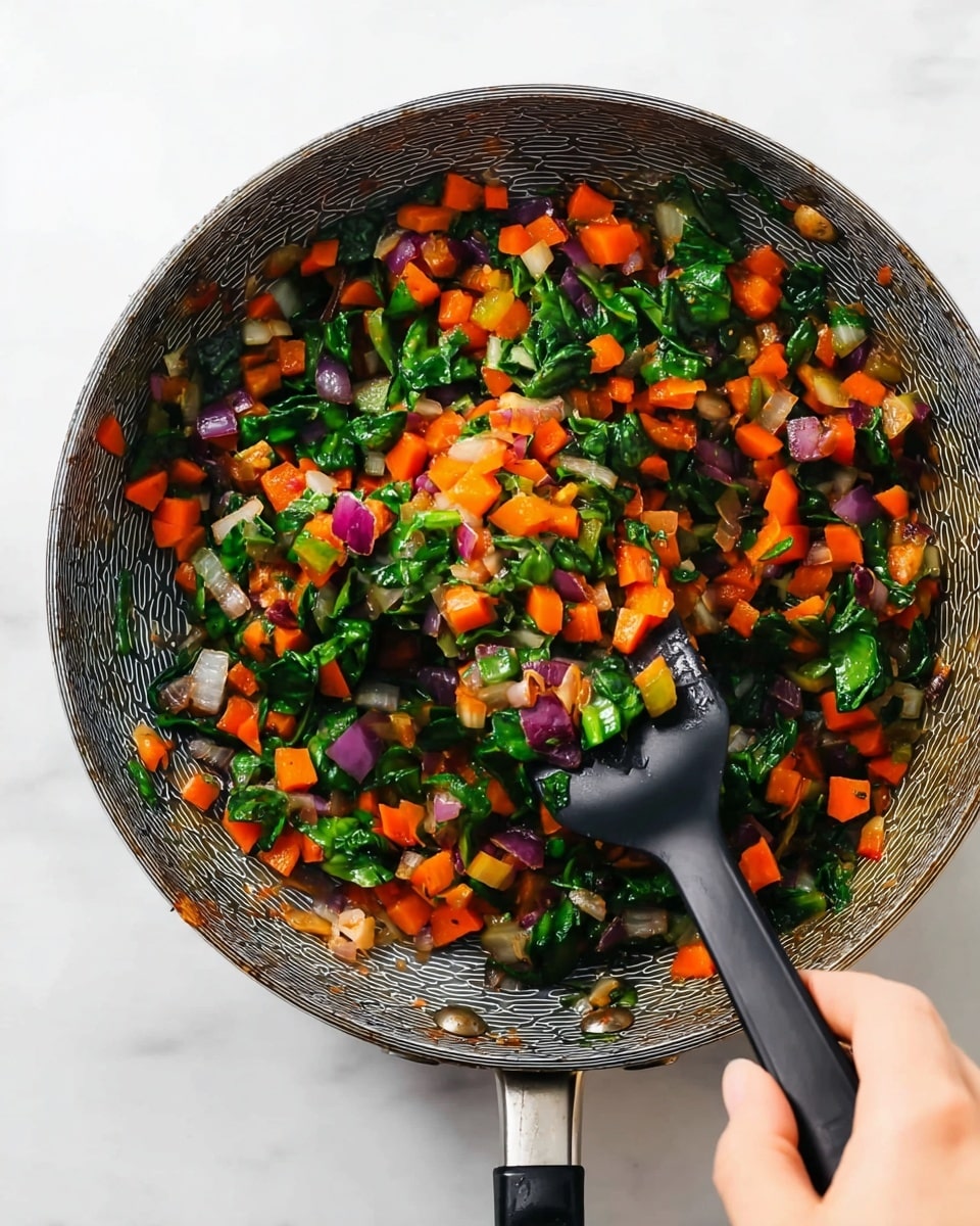 A close-up view of a frying pan with a black handle placed on a white marbled surface, filled with a colorful mix of small diced vegetables including bright orange carrots, deep green spinach leaves, and bits of purple and white onions. A woman's hand is seen holding a black spatula, lifting some of the sautéed vegetables, showing their soft texture and vibrant colors. The pan's interior has a subtle patterned texture that contrasts with the fresh, cooked vegetables inside. The image has a bright and clean look, focusing on the vibrant colors and textures of the ingredients. photo taken with an iphone --ar 4:5 --v 7