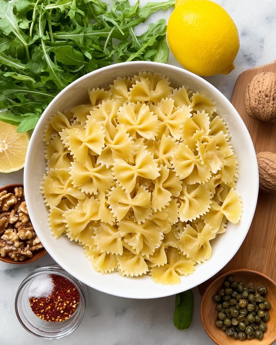 A large white bowl filled with uncooked farfalle pasta, each piece pale yellow with a smooth texture and ruffled edges, sits in the center on a white marbled surface. Around the bowl are fresh green arugula and basil leaves, a whole bright yellow lemon, a measuring cup with walnut halves, a small wooden dish with salt, black pepper, and red spice, and an open jar of capers. The colors are natural and fresh, with a mix of green, yellow, light brown, and white. photo taken with an iphone --ar 4:5 --v 7