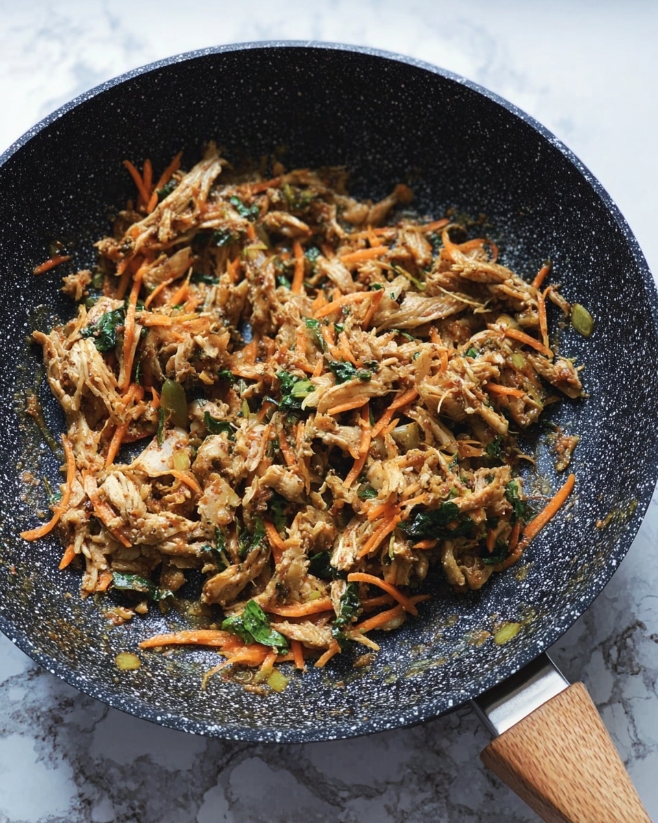 A black speckled pan with a wooden handle holds a cooked mix of shredded light brown meat and thin orange carrot strips, along with small pieces of green leafy vegetables scattered throughout. The mixture has a soft texture, and the background is a white marbled surface. Photo taken with an iphone --ar 4:5 --v 7