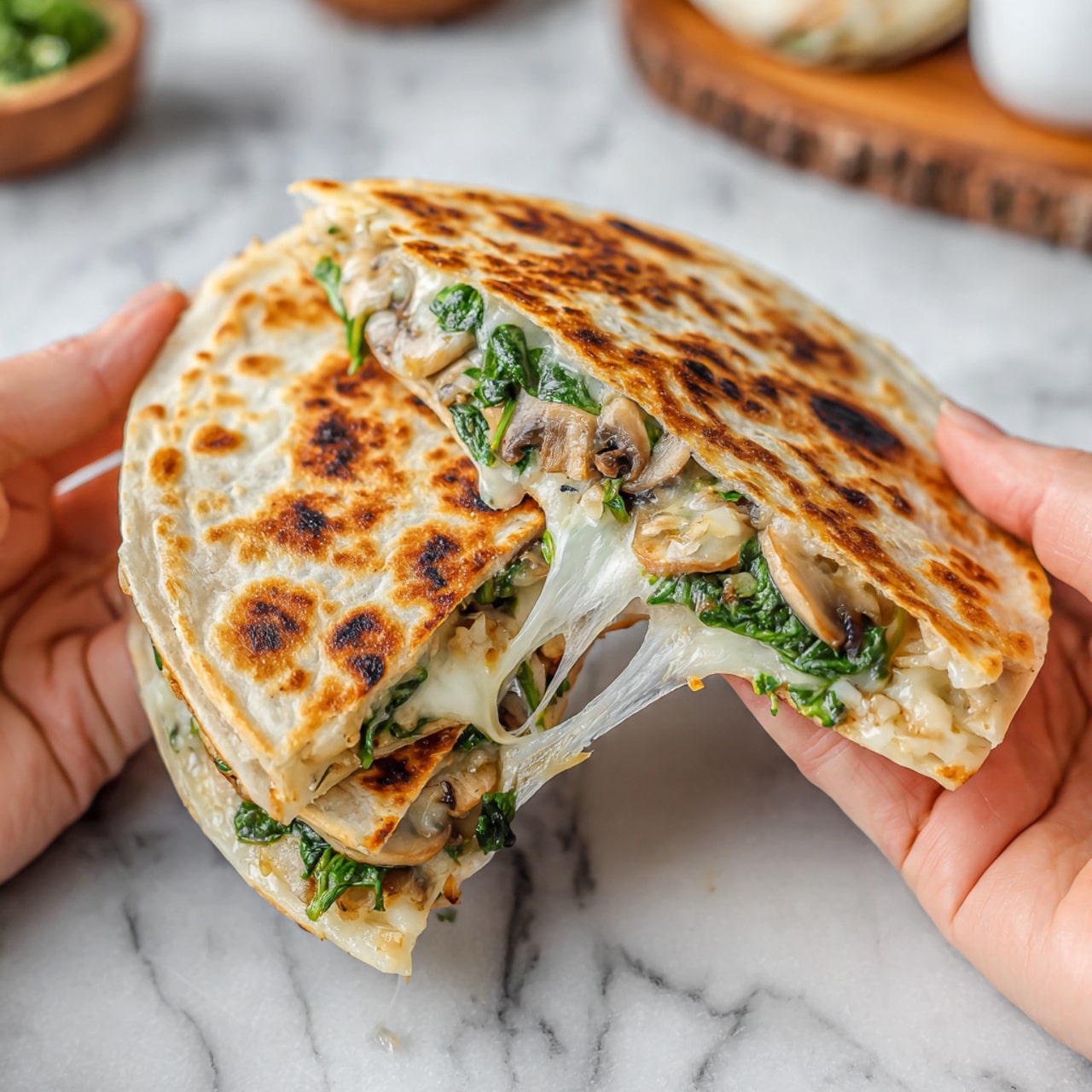 Two halves of a quesadilla are being pulled apart by two woman's hands showing the inside layers. The outer layer is a light golden-brown toasted tortilla with some darker charred spots. Inside, there are white melted cheese strands stretching between the two halves, mixed with chopped green spinach and small pieces of light brown mushrooms. The background is a white marbled surface with blurred kitchen items. Photo taken with an iphone --ar 4:5 --v 7