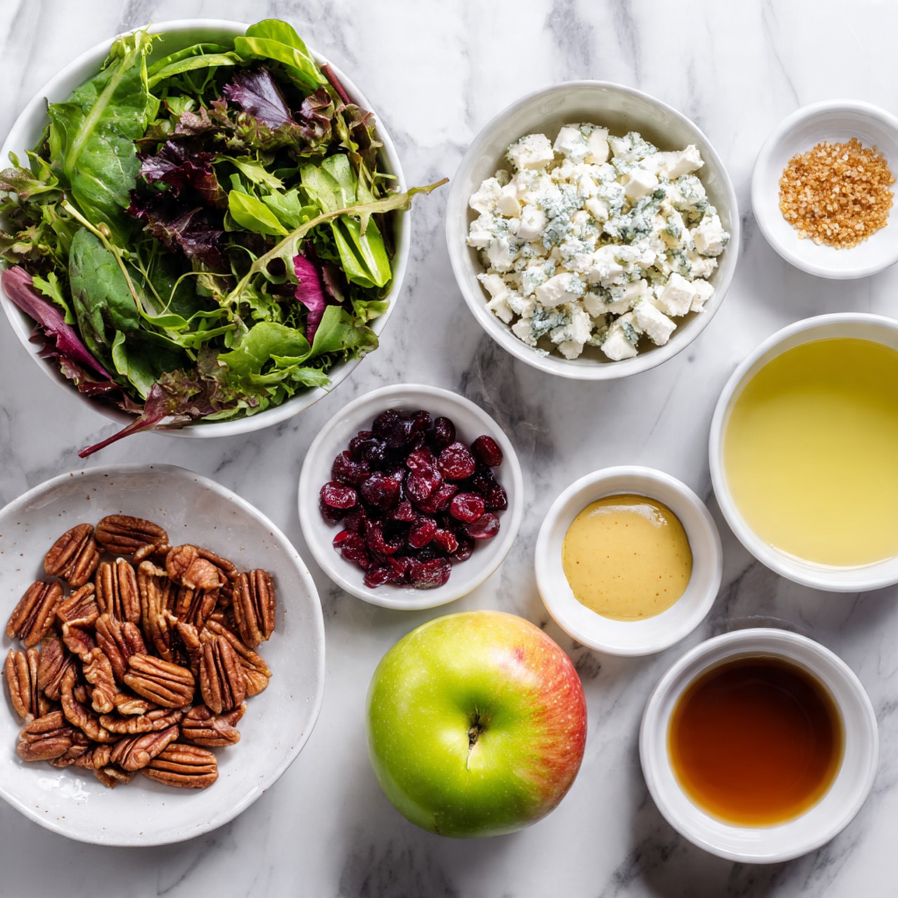 The image shows several white bowls and small dishes arranged on a white marbled surface, each holding different ingredients. At the top left, there is a large white bowl filled with mixed leafy greens in shades of dark green and purple. To the right, a white bowl contains crumbled white and light blue cheese. In the center, a white plate holds a whole green apple with red patches. Around these, smaller white bowls and dishes hold ingredients: reddish-brown pecans in one bowl, dark red dried cranberries in another, a small pile of yellowish granulated powder with salt on a speckled dish, a light yellow creamy mustard on another speckled dish, a small bowl with light liquid, a dark brown dish with a deep amber liquid, and a white bowl with a light yellow liquid. The composition is neat and clear, viewed from above. photo taken with an iphone --ar 4:5 --v 7